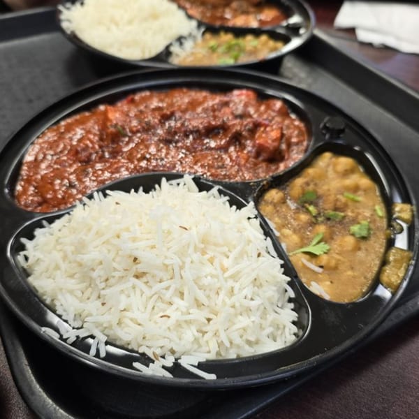 A Z Kabob platter with white rice, red curry, and chickpea curry in a black divided plate.
