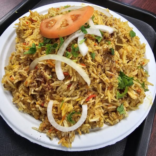 Z Kabob's chicken biryani with rice, sliced tomatoes, onions, and cilantro on a white plate.
