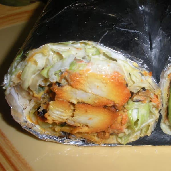 Close-up of a Z Kabob chicken wrap, with orange chicken, lettuce, and sauce, partially unwrapped.