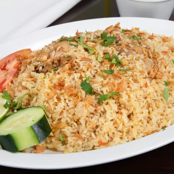 Z Kabob's chicken biryani with fried onions, cilantro, tomato, and cucumber on a white plate.